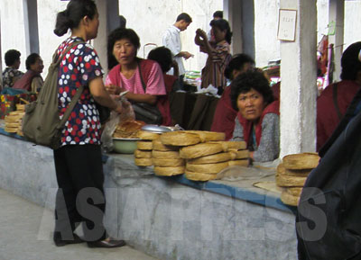 売場台に積み上げられているものが「人造肉」。帯状のものが巻かれて円盤になっている。北朝鮮の全国の市場でよく見かける食糧品だ。（2008年9月平壌市江東郡の公設市場　チャン・ジョンギル撮影）