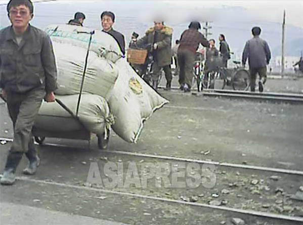 【写真3】　今にもこぼれ落ちそうなほどの荷を積んだリヤカーを引いて踏切を渡る男性。2013年3月平安南道平城（ピョンソン）市で 撮影 アジアプレス