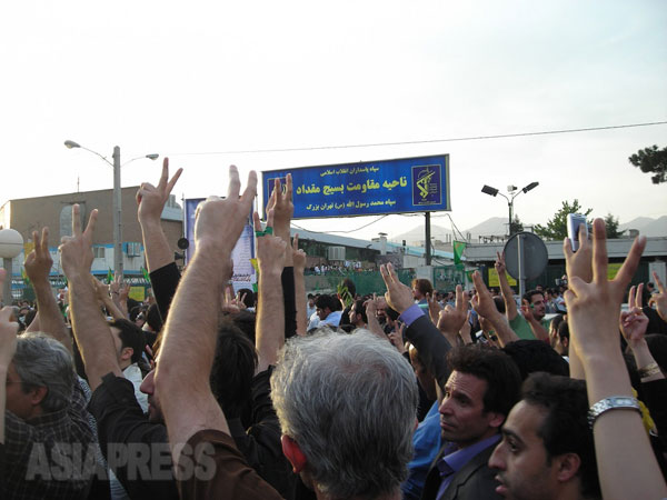 2009年6月15日にテヘランで行なわれた改革派のデモ行進。約50万人が参加。改革派弾圧に大きな役割を果たしたバスィージ（市民動員軍）の施設前でピースを掲げる改革派市民。日没後、一部で騒乱が発生し、改革派側に7人の犠牲者が出た。