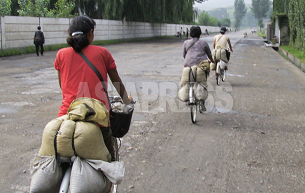 取締りを避けるために裏道を自転車で疾走する「テゴリ」の女性たち。農村から都市部に食糧を運搬している。2008年8月平壌市郊外の農村部で、撮影チャン・ジョンギル（アジアプレス）