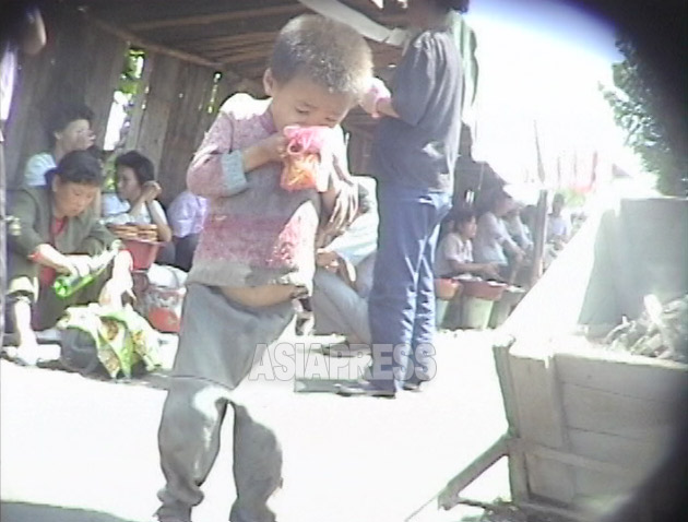 飢えたコチェビの男の子が、客の食べ残したソバの汁をビニール袋に入れてもらい食べている。1999年9月咸鏡北道茂山(ムサン)郡にて撮影キム・ホン(アジアプレス)