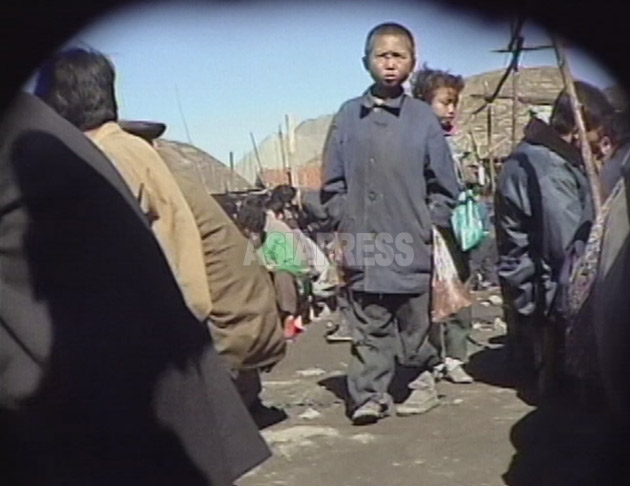 残飯を入れてもらうビニール袋を持って闇市場を徘徊するコチェビの少年たち。1999年9月咸鏡北道の茂山（ムサン）郡にて撮影キム・ホン（アジアプレス）