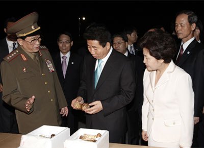 「金総書記の側近中の側近、朴在京（パク・ジェギョン）人民軍大将から土産の松茸を受取りご満悦な様子の盧大統領。今回北側が送った七宝山産松茸は500箱4トン！　「民衆の大統領」はこの日に合わせて動員された北の民の苦労に思いを馳せただろうか……。（2007年10月　韓国青瓦台HPより）