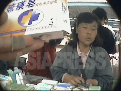 朝鮮の全てのジャンマダンは、中国製品に席巻されているような状態だ。清津の水南（スナム）市場の雑貨売り場で、撮影者のリ・ジュンが中国の薬品を手に取っている。（2004年7月撮影）