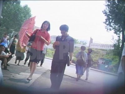流行りの短めの丈のスカートにハイヒール。真っ赤なブラウスに日傘。あか抜けた装いで目を引いた女性。（2007年8月平壌市　リ・ジュン撮影）
