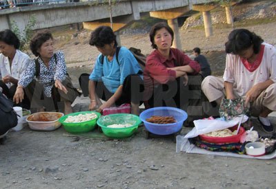 市場に向かう道で餅やパンなど自家製の食べ物を売る女性たち。別記事「内部記者が撮った！　北朝鮮最新事情　１」の若い兵士ほど痩せた人は見られない。商売で現金を得て食糧を買えるからだ（リンク先を参照した後この記事に戻るには、ブラウザの戻るボタンを押してください）。（2008年9月　チャン・ジョンギル撮影）