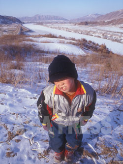 満13歳にして身長110センチだった孤児のソクチョル君は、一人で豆満江を越えて中国に渡った。朝鮮族の教会に保護されていた。後ろは凍結した豆満江。（2001年1月中国延辺朝鮮族自治州　石丸次郎撮影）