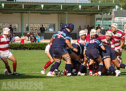 ▲写真は高校ラグビー大阪地区予選の決勝戦に挑む朝鮮高級学校チーム (2006年)。赤白ストライプのユニフォームが朝高の選手。この試合には敗退したが、高校サッカーでは全国大会出場を果たすなど強豪として知られる。撮影：アジアプレス