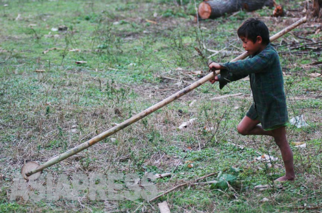 男の子が、先端に木製の車輪の付いた竹竿を懸命に転がす。
