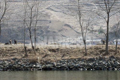 住民が稲わらを背負いどこかに運んでいる。後ろに禿山が見える。