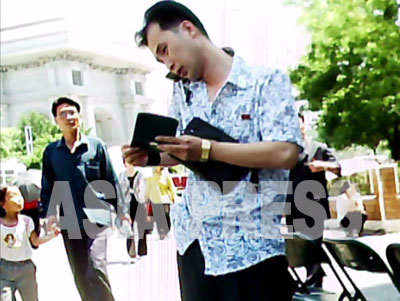 手帳をめくりながら携帯電話を使う男性。場所は平壌市の中心部、背後に凱旋門が見える。（2011年6月牡丹峰（モランボン）区域　ク・グァンホ撮影)