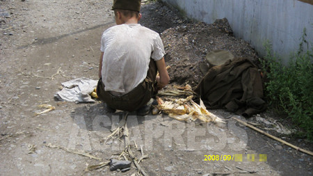 畑で盗んだトウモロコシの皮を剥く兵士。痩せているのが分かる。2008年8月　撮影：張正吉（チャン・ジョンギル）(C)アジアプレス