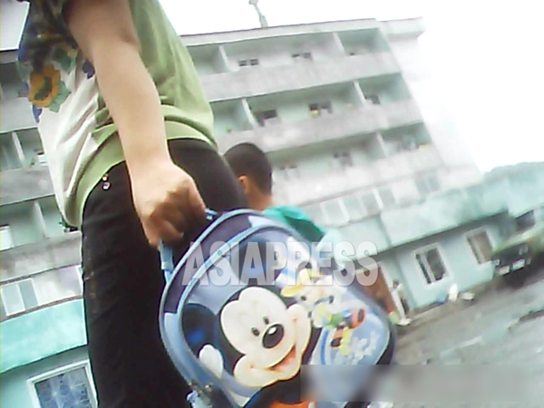 こちらも親子連れ。母が持つ子ども用のカバンにミッキーマウスが大きくあしらわれている。2013年8月、北朝鮮北部の朝中国境都市、撮影 アジアプレス 