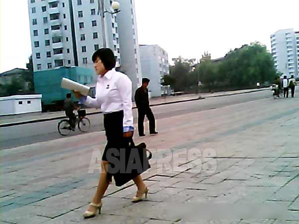 本を見ながら歩く女子大学生。シャツは最近流行の体にぴったりとフィットするタイプのもので規定から外れている。ハイヒールも履いているが、これは規定違反ではないとのこと。2013年9月平安南道平城（ピョンソン）市で撮影。写真アジアプレス