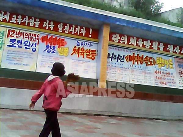 街頭の掲示板には、金正恩政権が打ち出した義務教育12年制を宣伝する文句が並ぶ。（ 2013年8月北朝鮮北部都市で 撮影アジアプレス）