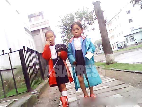 小学生の女の子二人が、雨上がりの道を歩いている。 (2013年9月北朝鮮北部都市で 撮影アジアプレス)