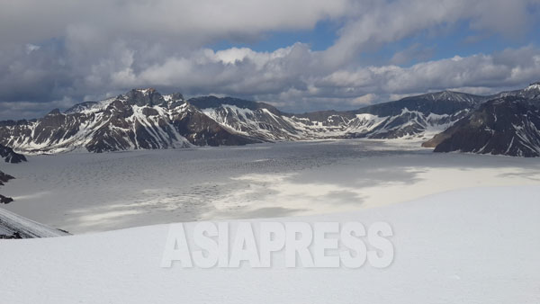 雪に覆われた白頭山頂上にあるカルデラ湖の天池。朝鮮民族発祥の伝説がある。北朝鮮側の山々が見える。5月下旬　撮影 朴永民／アジアプレス