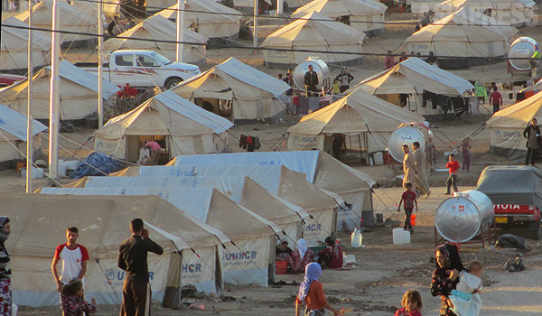 【イラク・クルディスタン地域】 こちらはイラク・クルディスタン地域の避難民キャンプ。６月に制圧されたイラク第２の都市モスルからの脱出民に加え、８月のシンジャル攻撃でさらに避難民は急増。ヤズディ教徒だけでなく、イスラム教徒、キリスト教徒、トルコ系住民など避難民は数十万におよぶ。キャンプはどこも収容限界を超えていた。モスルに比べて物価の高いクルディスタン地域では、キャンプに入れない避難民が家を借りるにも経済的な負担が伴う。地元当局や国際機関の支援も行き届かない状態で、住居、食料、就労、子どもの学校などさまざまな面で影響が出ていた。避難民にのしかかるストレスに加え、地元住民との摩擦も生まれ始めていた。写真のキャンプはクルディタン地域のザホー郊外で撮影。テントにはUNHCRの文字が見える。（イラク北部・ザホーで ９月・玉本英子撮影）