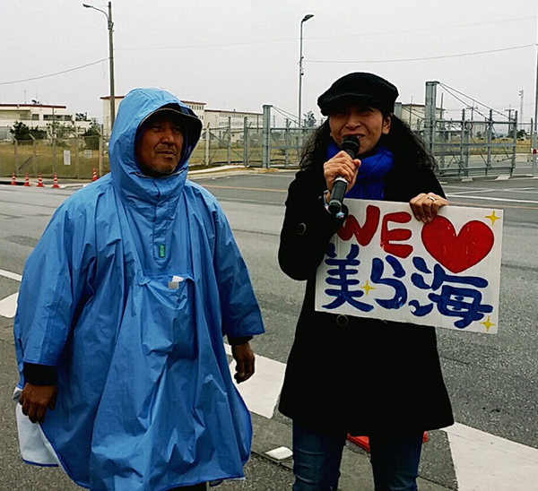 辺野古での新基地反対の抗議行動を指揮する山城博治さん㊧に紹介される城間真弓さん。夜中の資材搬入後、キャンプシュワブのゲート前での座り込みが24時間体制になる中、市民だけでは限界があると村長に直訴、村を動かし、読谷村からのバスの運行を実現させた。（撮影・栗原佳子）