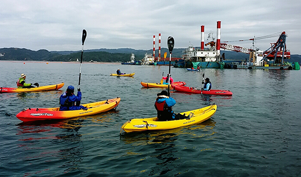 キャンプシュワブ沖にて。海上作業が行われず、海保のボートも出ていない静かな海。陸からの声援にパドルをあげて応えるカヌー隊（撮影・栗原佳子）