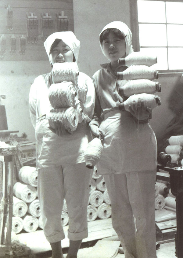 大阪・泉南地域のアスベスト紡織工場内でかつて撮影された記念写真。女性工員が手にしているのはアスベストでつくられた糸やひも。アスベストの危険性について教育もないため、防じんマスクもせず、カメラに笑顔を向けている（泉南地域の石綿被害と市民の会提供）