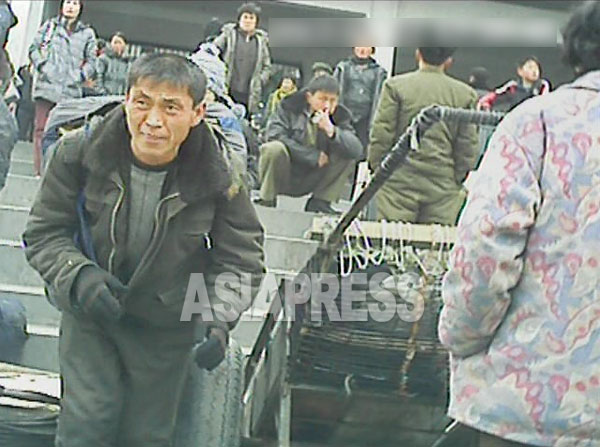駅前には乗降客目当ての運搬業者がひしめき合う。客の大荷物を背負った男性（左）が階段を駆け下りてきた。（2013年3月平安南道平城（ピョンソン）市　ペク・ヒャン撮影）