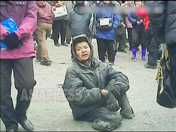 平安南道平城（ピョンソン）市の市場入り口に座り、食べ物とお金を乞うコチェビの少年。両足首が無い。2013年3月。