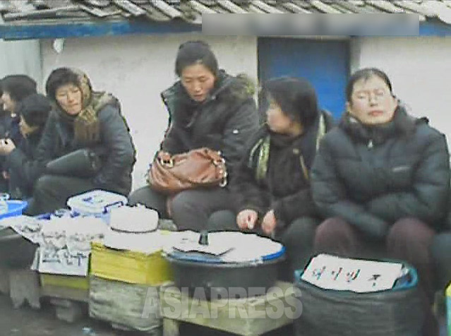 アパート街の通りにずらりと並ぶ食べ物売りの女性たち。右は「豚足」、左は「ギョウザ・饅頭」。2013年3月平安南道平城市(アジアプレス)