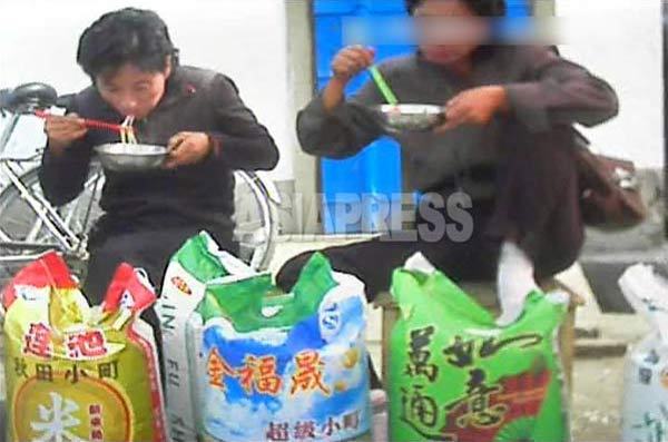 中国産のコメを売る女性たちがソバで腹ごしらえしている。コメの袋には「秋田小町」の商標が。2013年10月北部国境都市。(撮影アジアプレス)