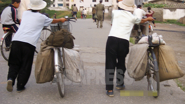 商売を終えた帰路か、仕入れから戻ったところか、大荷物を載せた自転車を押す 二人の女性。2008年8月平壌市郊外でチャン・ジョンギル撮影（アジアプレス）