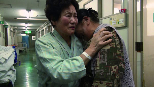 菅野芳子さん（左）が入院し、不安の中、見舞いに訪れた榮子さん。仮設住宅でひとり暮らしの榮子さんにとって、芳子さんの存在はなくてはならないものになっていた。（映画「飯舘村の母ちゃんたち　土とともに」より） 