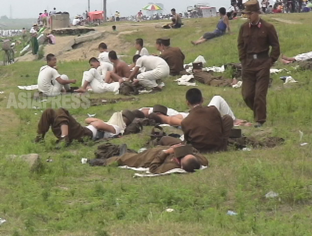 河川敷の公園で休憩時間に力なく寝そべる兵士たち。2006年8月清津市にてリ・ジュン撮影（アジアプレス）