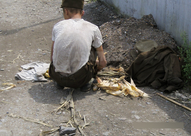 後姿のシャツにうつった浮いたあばら骨が痛々しい。脇にはくたびれた軍服と軍帽が。2008年8月平壌市郊外にて撮影チャン・ジョンギル(アジアプレス)