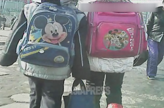 下校途中の小学生二人。左はミッキーマウス、右は不明。中国から入る衣類やかばんを通じて外国の情報に幼い頃から触れる。2012年11月平安北道新義州(シニジュ)市にて撮影アジアプレス
