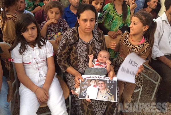 ヤズディコミュニティでは親族や知人の誰かが犠牲となった。追悼集材でISによる虐殺の犠牲者の写真を手にする女性。（イラク北部・8月2日）