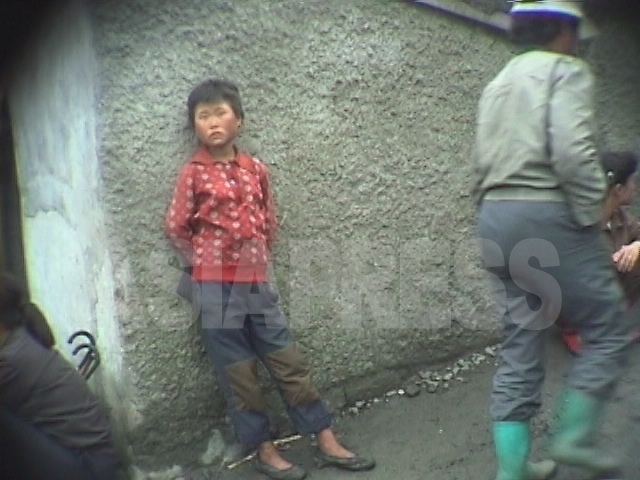 闇市場の中で、中学生ぐらいの少女が何する風でもなくじっと立っている。ひどく痩せている。1998年10月江原道元山(ウォンサン)市にて撮影アン・チョル(アジアプレス) 