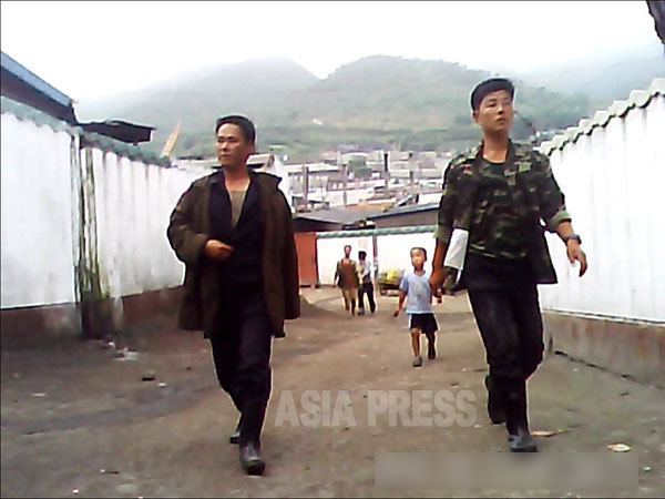 路地裏を闊歩する二人組。右の男性が着る迷彩色のシャツと上着は軍服だが、市場でも売っている。2013年9月咸鏡北道の清津市（チョンジン）市にて撮影「ミンドゥルレ」（アジアプレス）