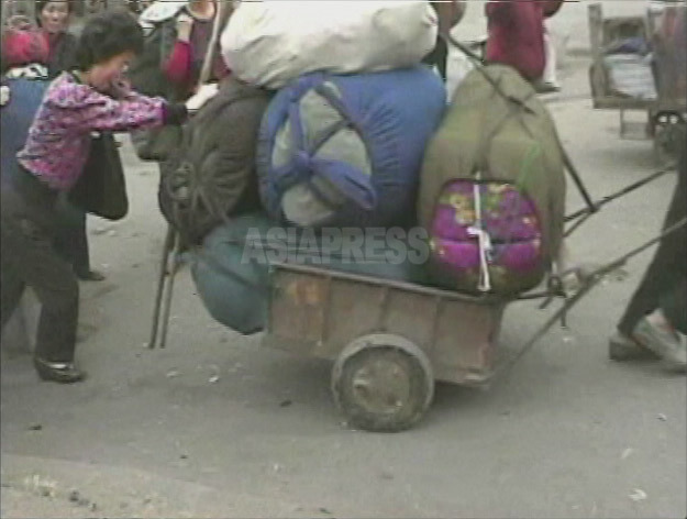 開場する市場に向かって大荷物を運ぶ女性。布団のようなものが見える。多く家庭は女性の商行為の収入に生計を頼る。2008年10月黄海南道海州（ヘジュ）市にて撮影シム・ウィチョン（アジアプレス） 