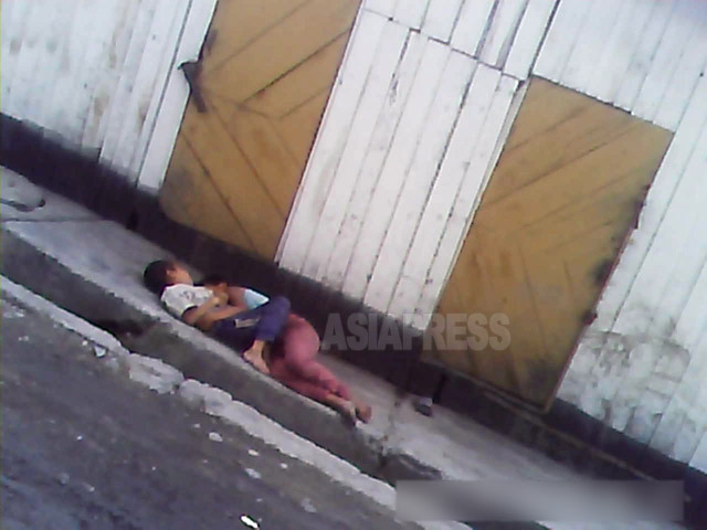 姉弟だろうか、女の子と小さな男の子が市場近くの倉庫前で抱き合って寝ていた。靴もなく裸足である。2013年8月両江道の恵山市にて撮影アジアプレス