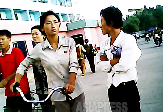自転車を押す女性の胸には金日成バッジ。2013年9月平安南道平城市にて撮影アジアプレス