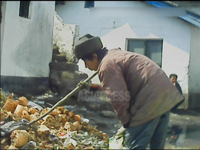 アパート街のゴミ捨て場で使えそうな物を探す男性コチェビ。2013年3月平安南道平城市にて撮影アジアプレス。 