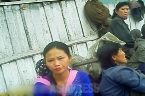 若い母親が赤ん坊を負ぶって路地で商売をしている。東部の咸鏡南道の高原郡にて2012年8月撮影「ミンドゥルレ」(アジアプレス) 