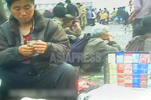 商売をする人でごった返す道路でたばこを売る女性。札を数えている。2012年8月両江道恵山市にて撮影「ミンドゥルレ」(アジアプレス) 