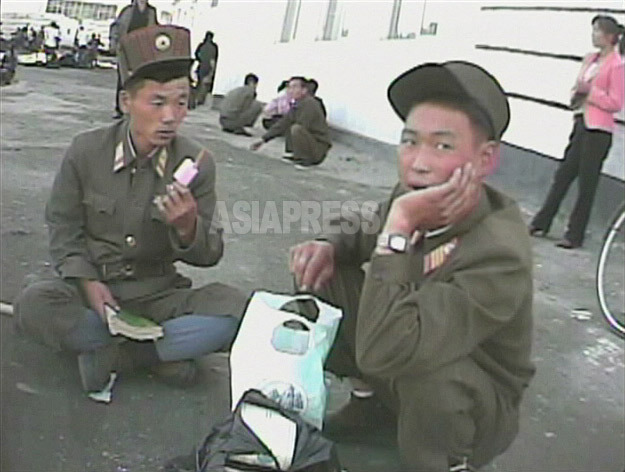 部隊の移動の途中で道に座り込んだ兵士が食べているのはアイスキャンデー。商売人たちが自家製を売る。2008年9月黄海南道海州市にてシム・ウィチョン撮影(アジアプレス) 