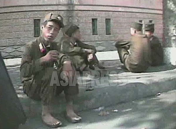 駅前で部隊の移動を待機中の兵士たち。足が蒸れるからか靴を脱いでいる。2008年10月黄海北道の沙里院市にて撮影シム・ウィチョン（アジアプレス） 