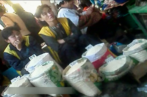 손님을 기다리는 여성 쌀 장사꾼. 쌀 이름과 가격표가 놓여 있다. 대부분 4천원에서 5천원대로 적혀 있다. 2012년 11월 양강도 혜산 시장에서. 아시아프레스 촬영
