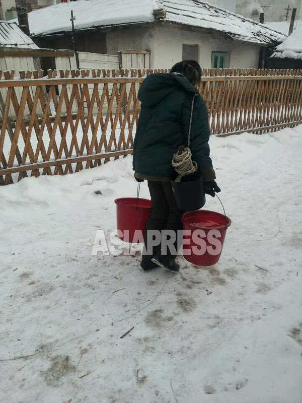 지방도시에서는 전기, 수도 사정의 악화로 주민의 불만이 커지고 있다. 사진은 마을 공동 우물에서 물을 긷고 집에 돌아가는 여성. 2015년 1월 북한 중부 지방에서 (민들레 촬영. 아시아프레스)