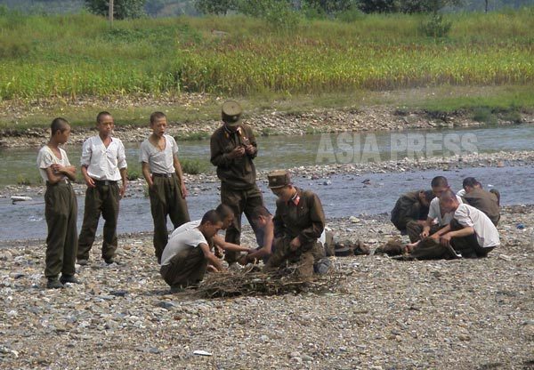 훔쳐 온 옥수수를 굽기 위해 강변에 불을 붙이는 병사들. 팔이 가늘다. 2008년 8월 촬영 장정길 (아시아프레스)