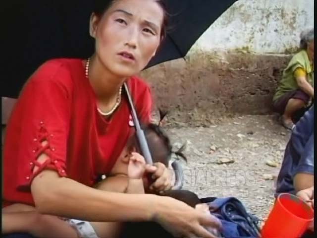 젖먹이를 데리고 노상에서 떡이나 빵을 파는 여성. 양산과 화장은 잊지 않는다. 2007년 황해북도 사리원시에서 촬영. (아시아프레스)