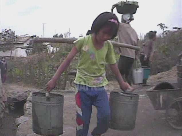 물이 가득 찬 물지게를 힘겹게 지고 일어서는 소녀. 2008년 10월 황해남도에서 촬영 심의천(아시아프레스)